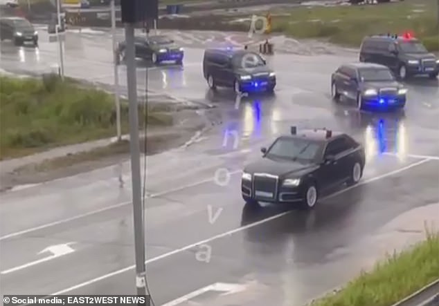 Footage shows a long line of black armoured vehicles speeding along a road, flanked by flashing police cars