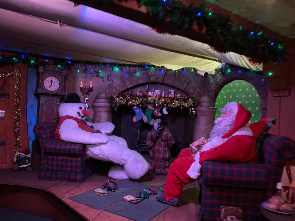 Santa Claus and a snowman sitting in armchairs by a fireplace.