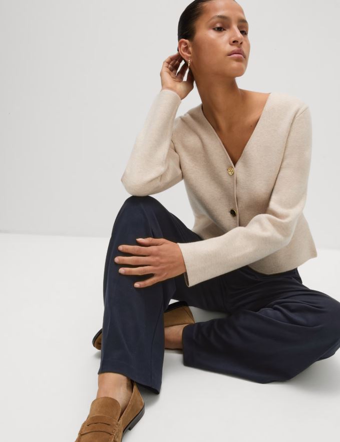 Woman sitting wearing navy trousers and a beige cardigan.