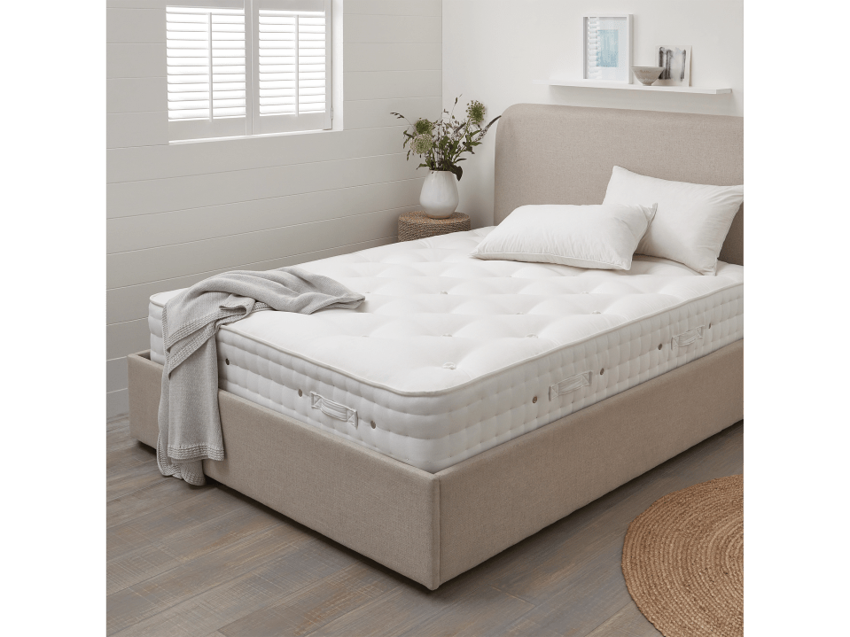 A beige upholstered bed with a white mattress and pillows.