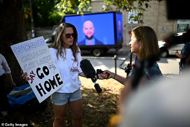 A woman holds a sign demanding Vance 'go home' as she demonstrates in Charlbury, Oxfordshire