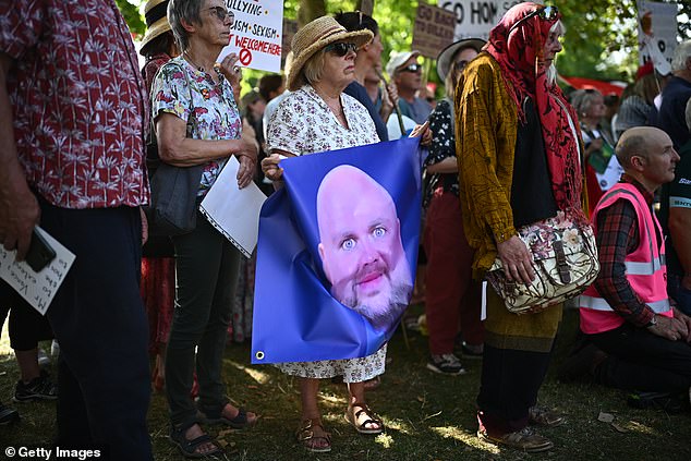 A woman holds a flag displaying the JD Vance meme showing the politician with exaggerated features and an egg-shaped head