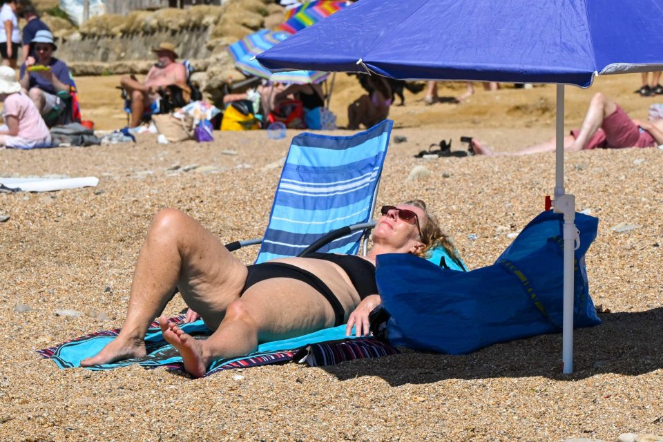 Woman sunbathing on a beach under a blue umbrella.