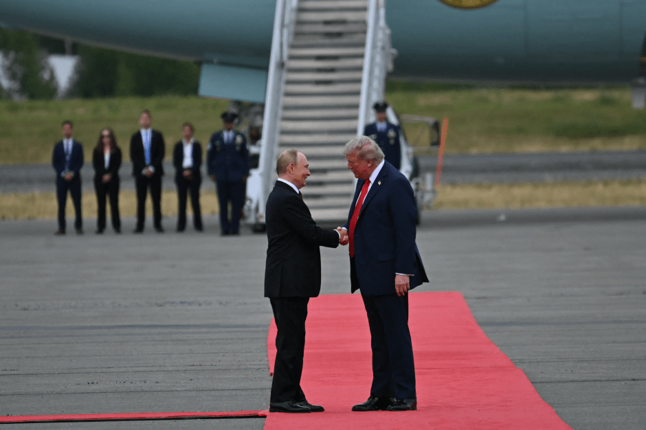 Putin and Trump shaking hands on a red carpet.