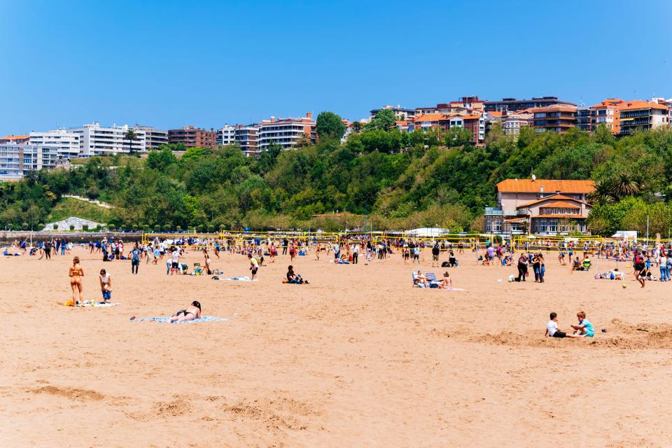 Crowded sandy beach with people playing volleyball.
