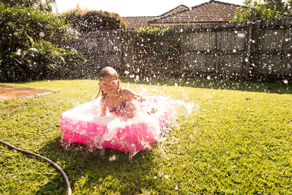 Girl splashing in a pink baby pool in a backyard.