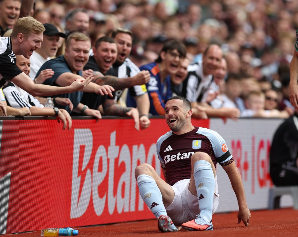 Aston Villa player John McGinn sits on the ground as Newcastle United fans taunt him.