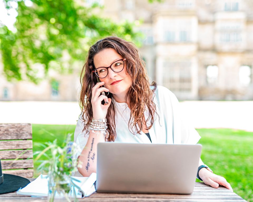 Woman on phone call working on laptop outdoors.