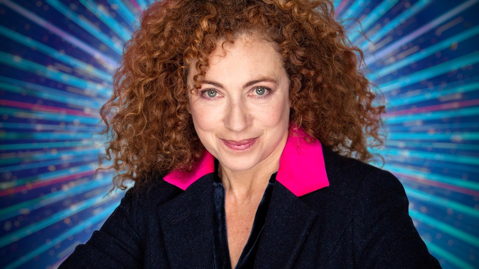 Portrait of a woman with curly red hair, wearing a dark jacket with a bright pink collar.
