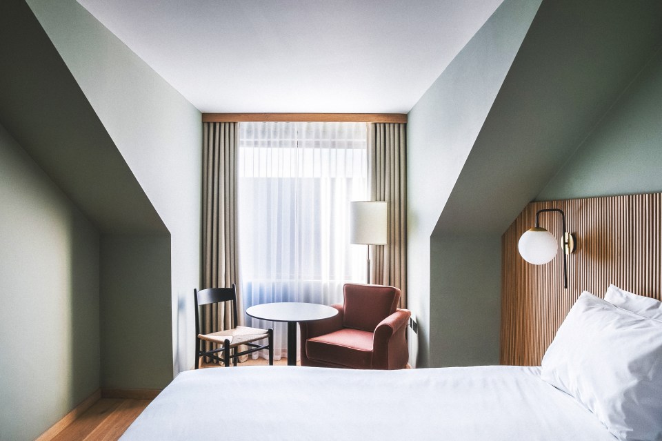 Hotel room with a bed, armchair, and small table.