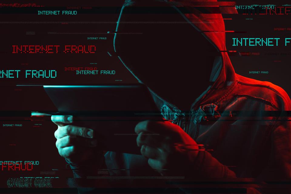 Hooded figure using tablet, text overlay: Internet Fraud.