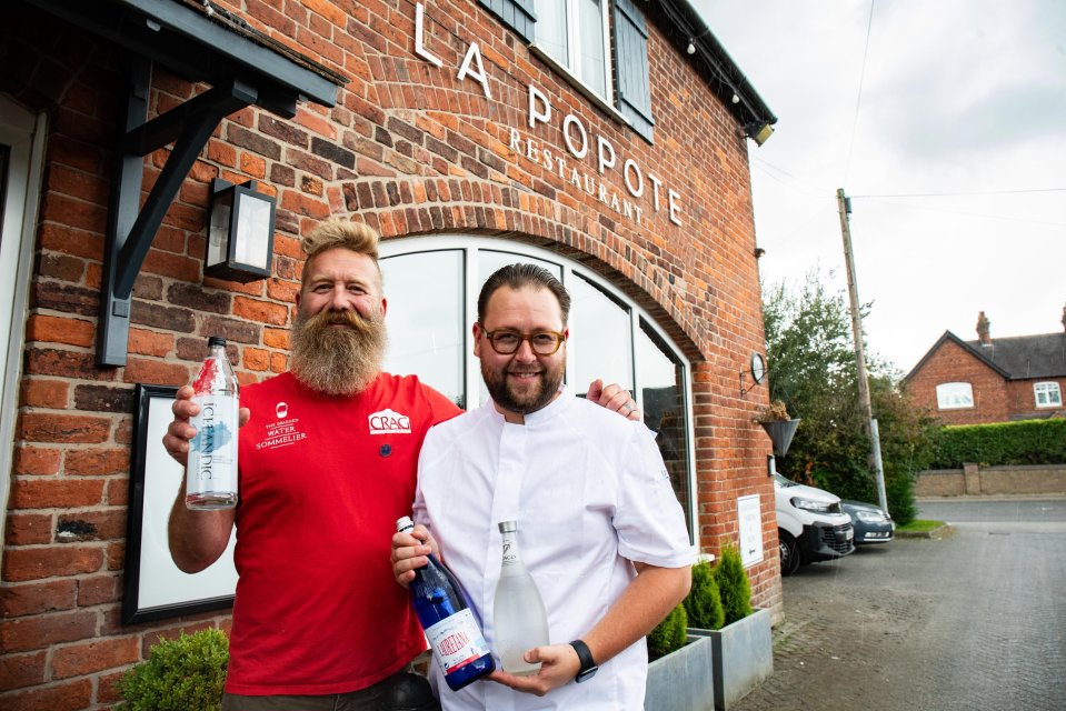 Two men outside La Popote restaurant holding bottles of water from their bottled water menu.