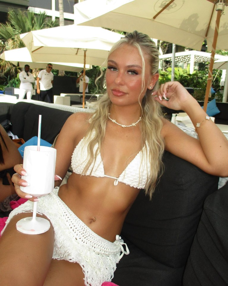 Woman in white bikini and cover-up holding a drink.