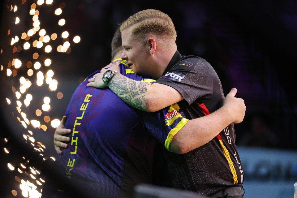 Mike De Decker of Belgium congratulates Luke Littler of England after a darts match.