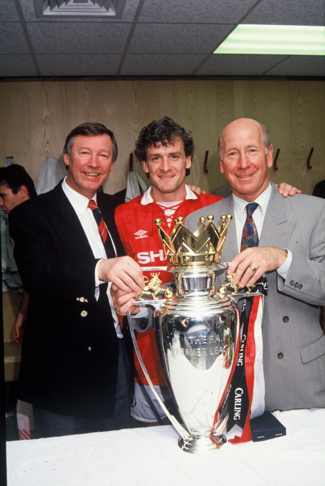 Sir Alex Ferguson, Mark Hughes, and Sir Bobby Charlton holding the FA Premier League trophy.