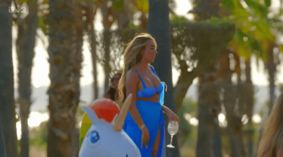 Woman in blue bikini and cover-up walking by inflatable unicorn.