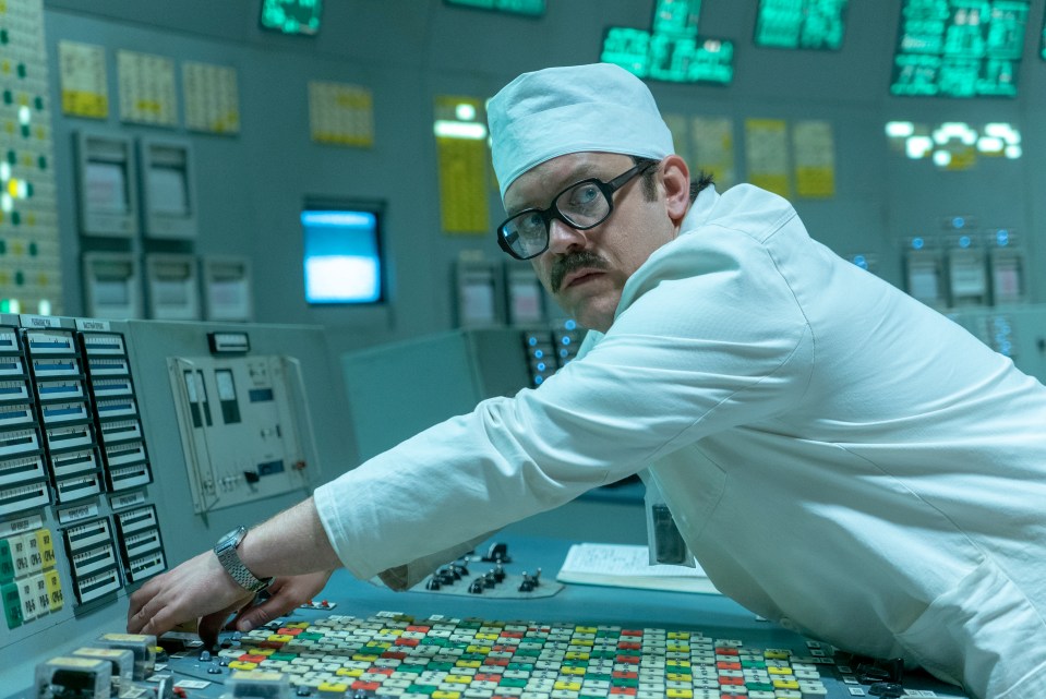 Man in a white lab coat operating a control panel.