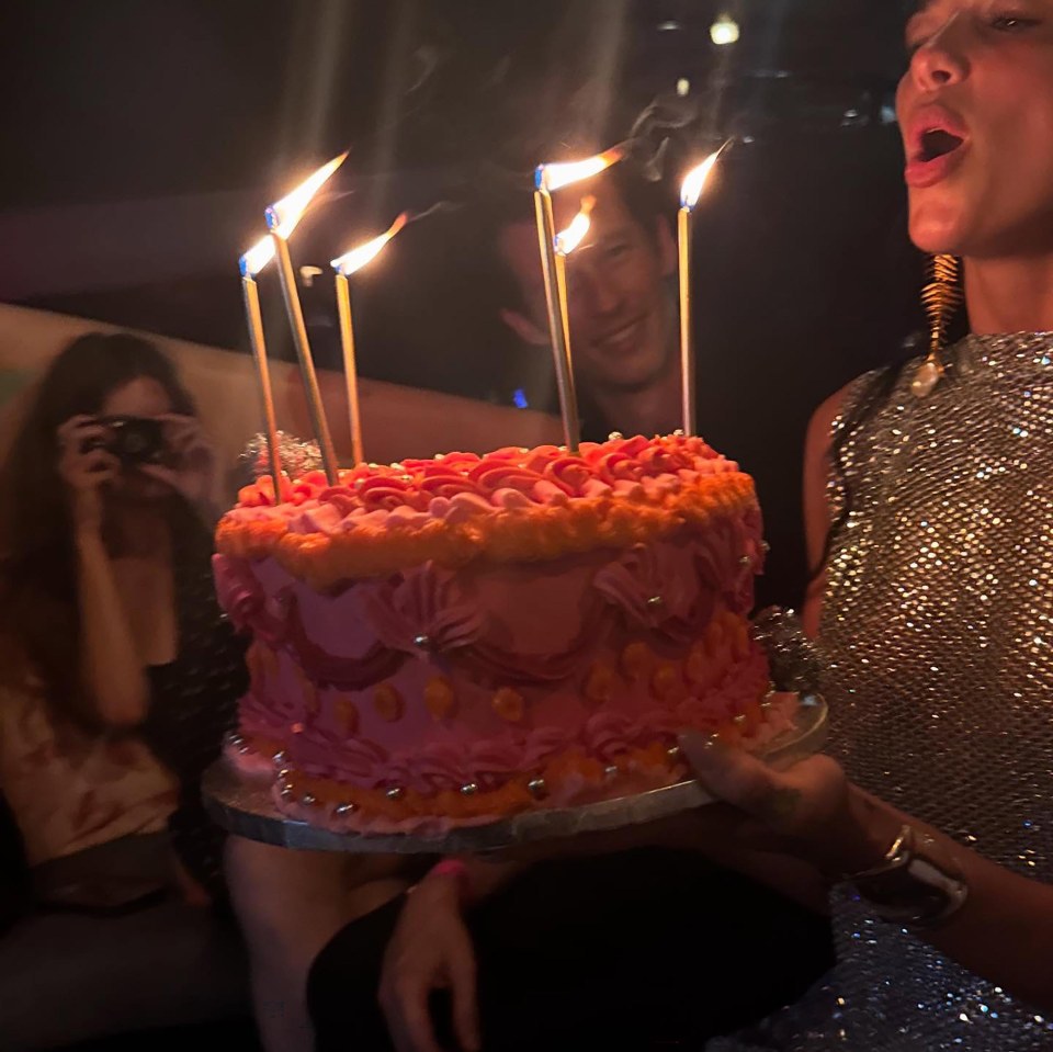 Dua Lipa holding a pink and orange birthday cake with lit candles.