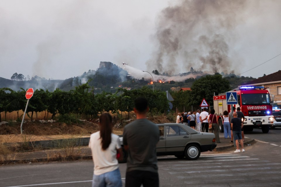 Plane dropping water on a wildfire near onlookers.