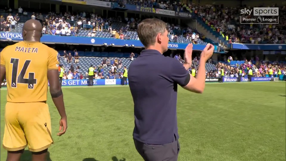 A soccer player with his back to the camera and a man clapping in a stadium.