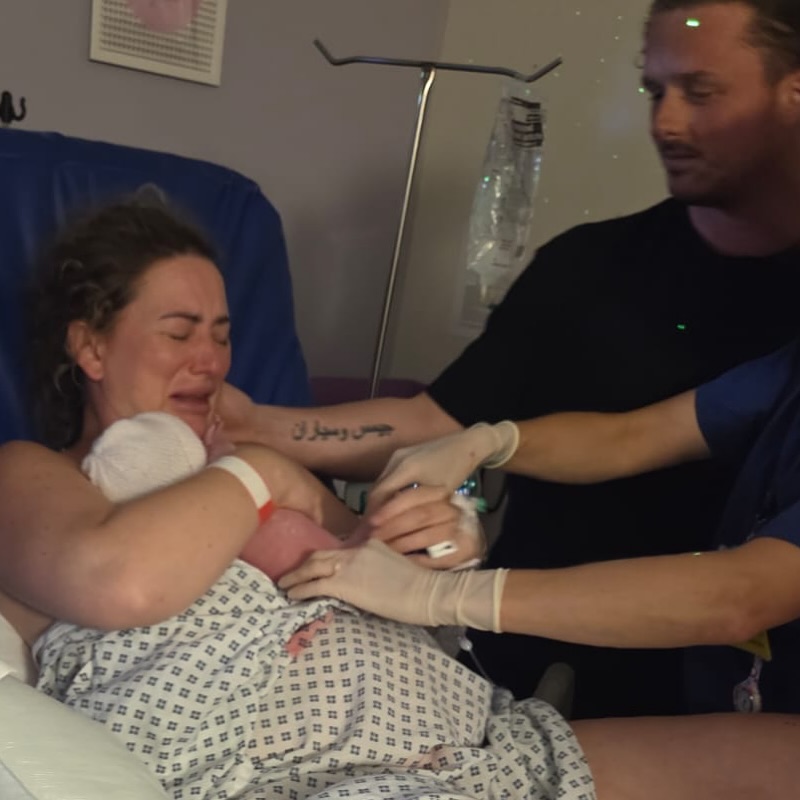 Mother holding newborn baby, crying, with father and medical staff present.