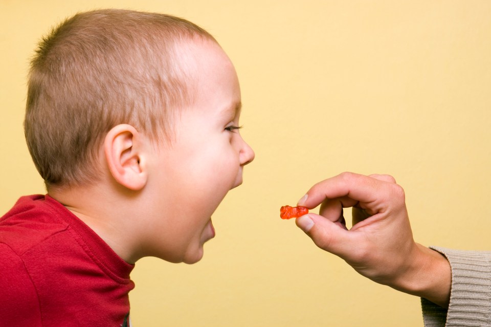 A toddler eagerly anticipates a gummy candy being offered to him.