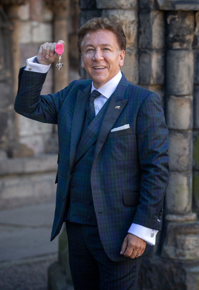 Ross King smiling and holding his MBE medal.