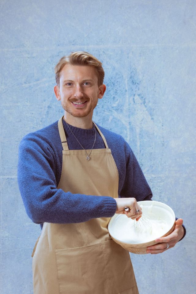 Smiling man wearing an apron whisking cream in a bowl.