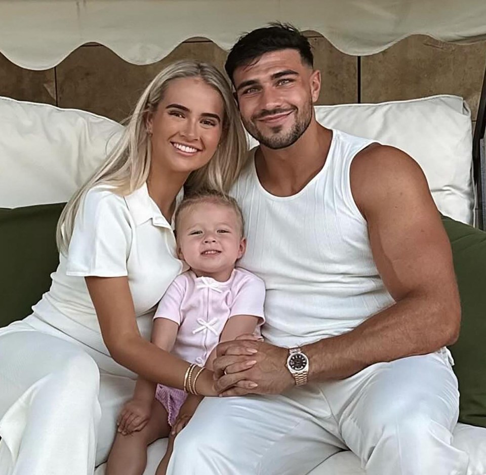 Tommy Fury, Molly Mae, and their baby daughter sitting together on a patio swing.