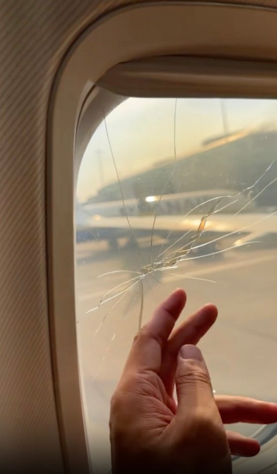 Cracked airplane window with a hand touching it.