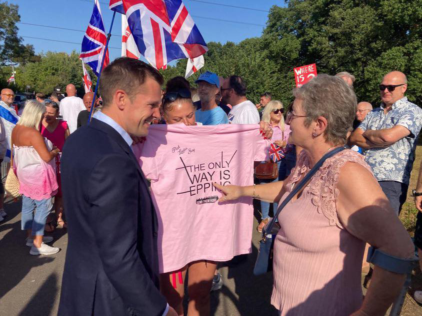 Robert Jenrick at an Epping protest, shown being presented with a pink t-shirt.