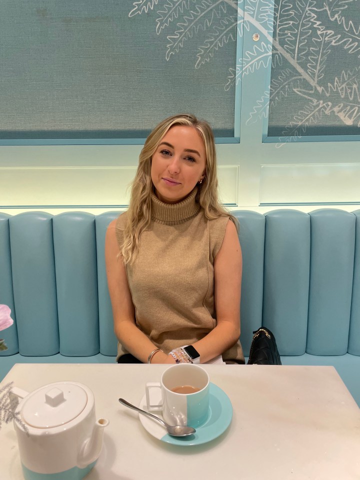 Woman sitting on a teal booth in a cafe drinking tea.