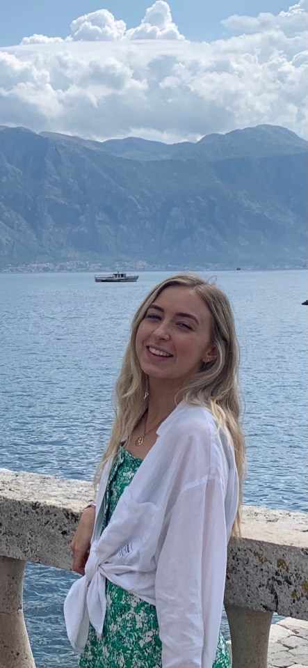 Woman smiling by the sea with mountains in the background.