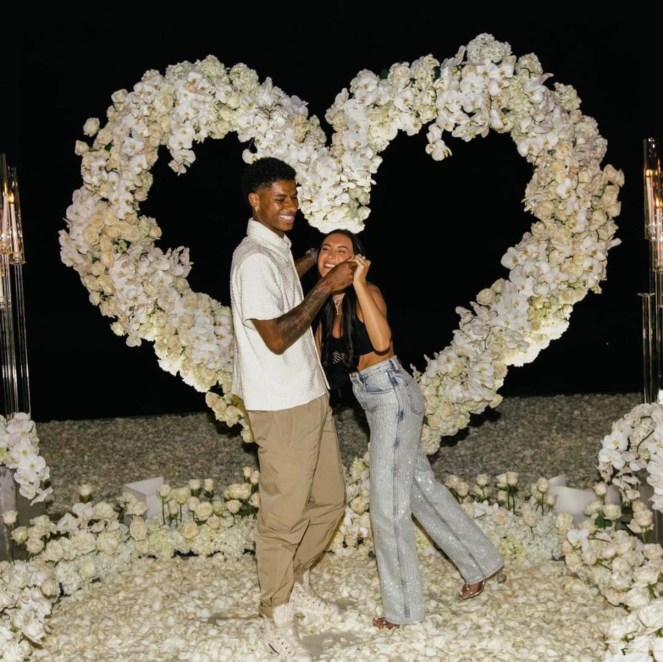 Couple smiling together in front of a heart-shaped floral arrangement.