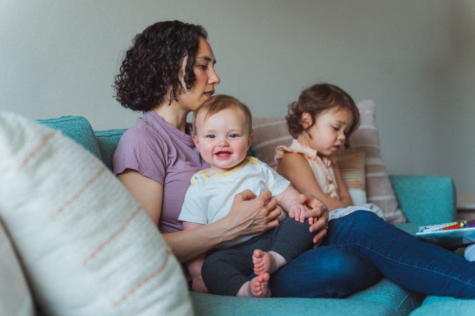 A mother reading a book to her two young children on a sofa.