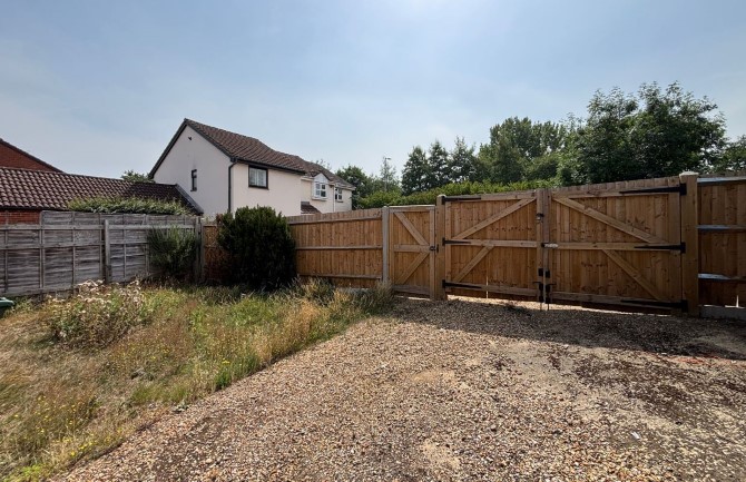 Photo of a bungalow's overgrown garden and wooden gate.