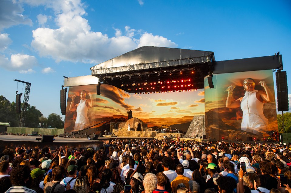 Large crowd at an outdoor music festival watching a performance on a main stage.
