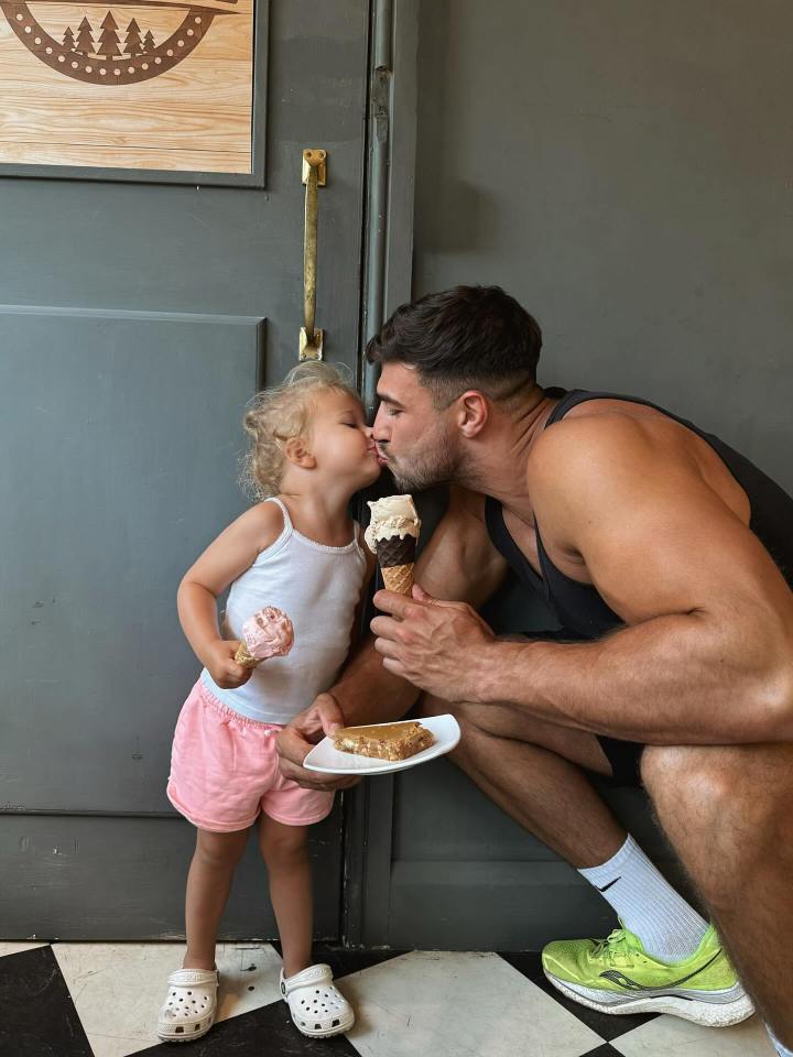 A man kisses a toddler while holding ice cream cones; a dessert sits on a plate nearby.