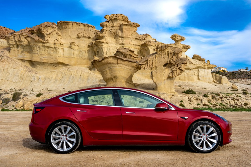 Red Tesla Model 3 parked near a rock formation.