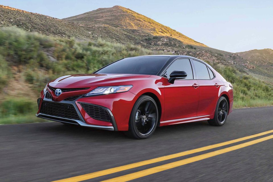 Red 2024 Toyota Camry Hybrid driving on a road.