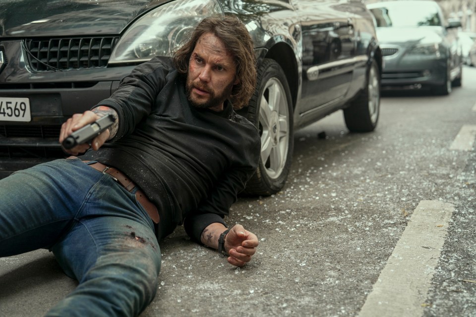 Injured man holding a gun on the ground.