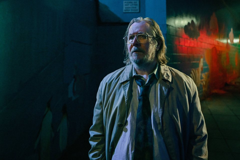Man in glasses and trench coat standing in an alleyway at night.