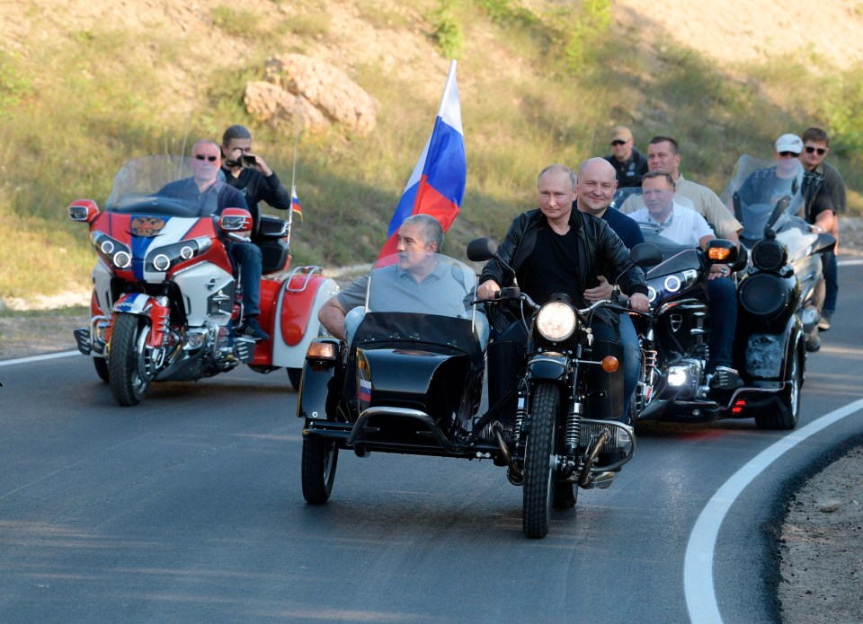 Vladimir Putin driving a motorcycle with Sergei Aksenov in a sidecar.