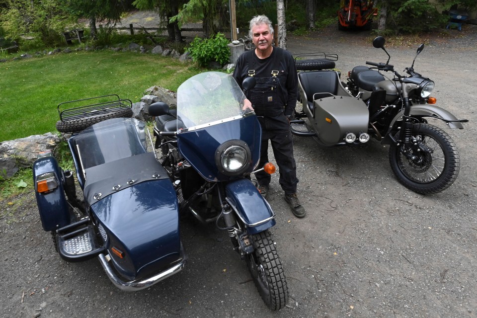Man standing between two Ural motorcycles with sidecars.