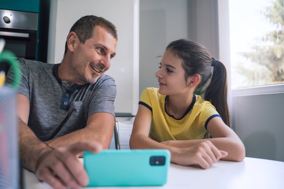A father and daughter smiling while looking at a smartphone together.