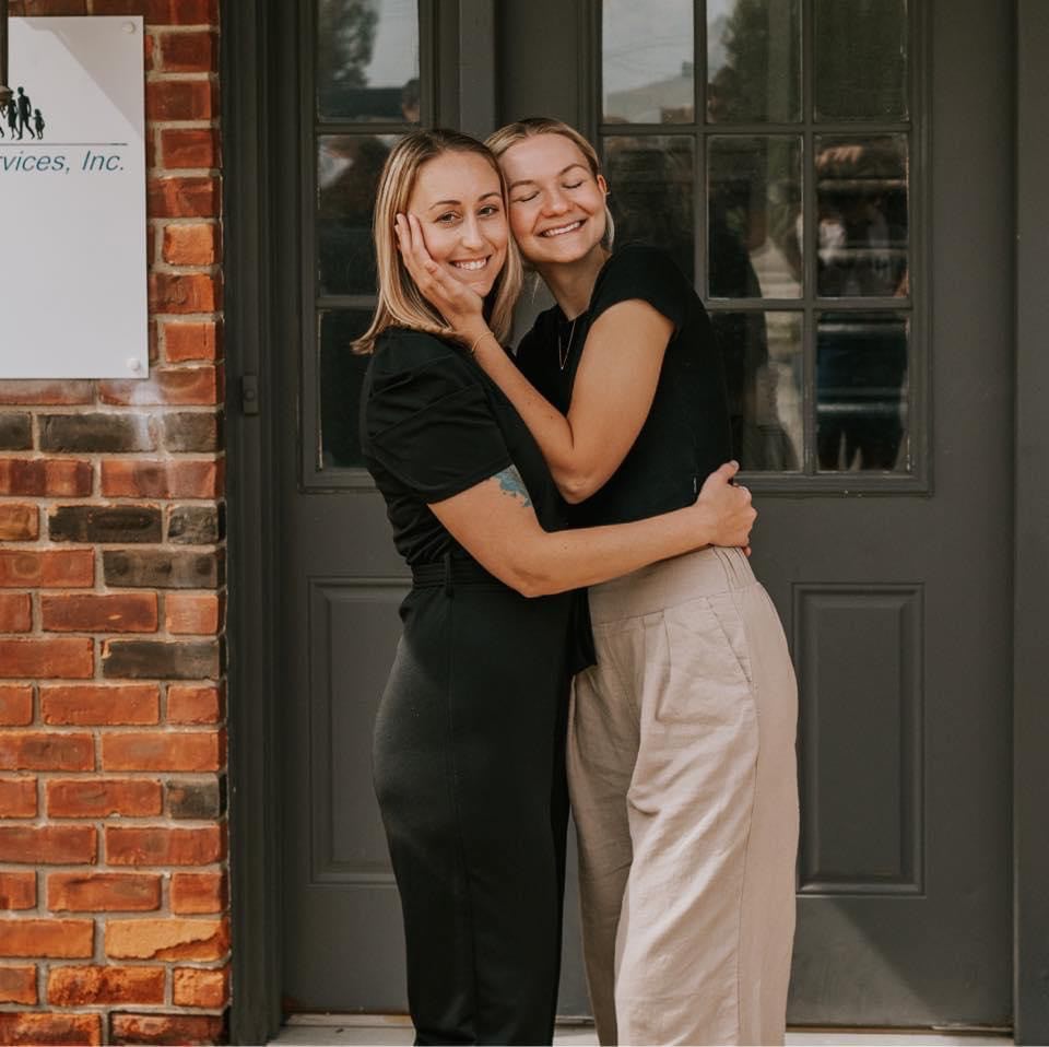 Two sisters hugging in front of a building.