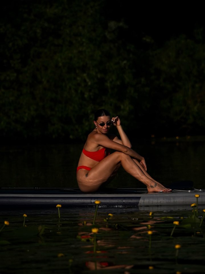 Woman in red bikini sitting on paddleboard on calm water.