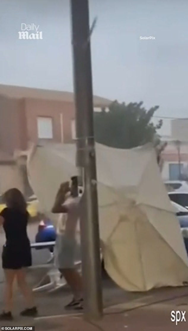 A woman was filmed holding a giant bar terrace parasol as the tornado swept away chairs and street rubbish containers behind her