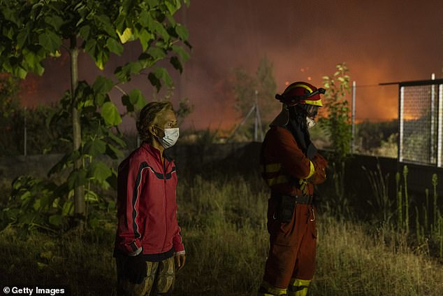 A member of the Emergency Military Unit (UME) and a citizen watch as a bulldozer arrives to protect a house from a wildfire on August 19, 2025 in the Ourense province, Spain