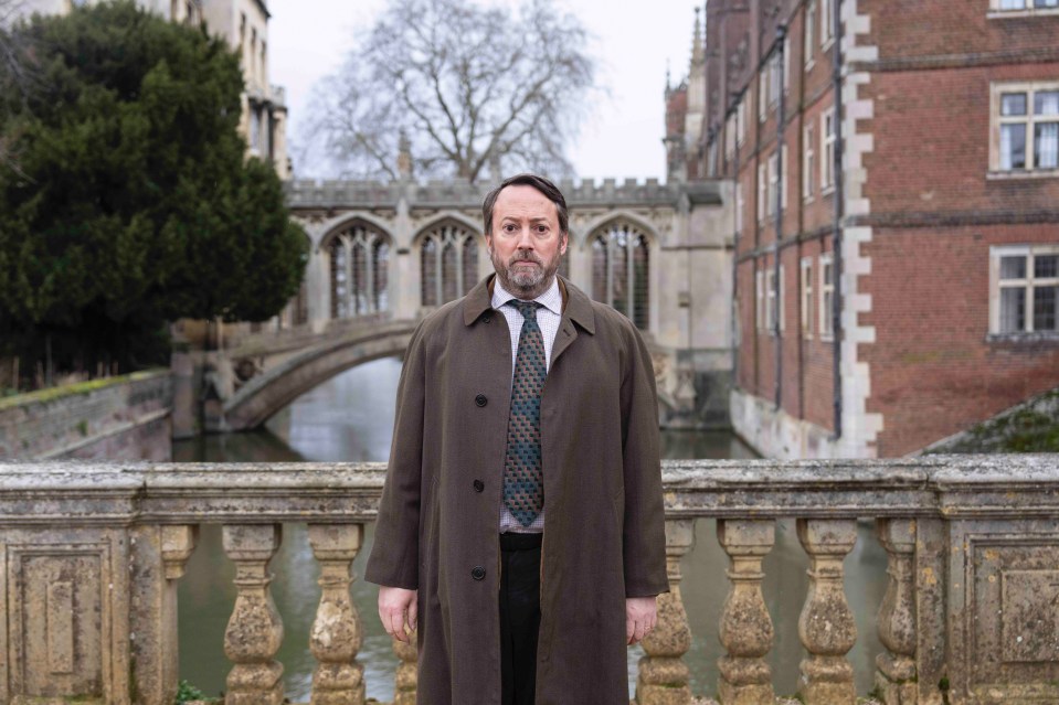 A man in a brown coat stands on a bridge.